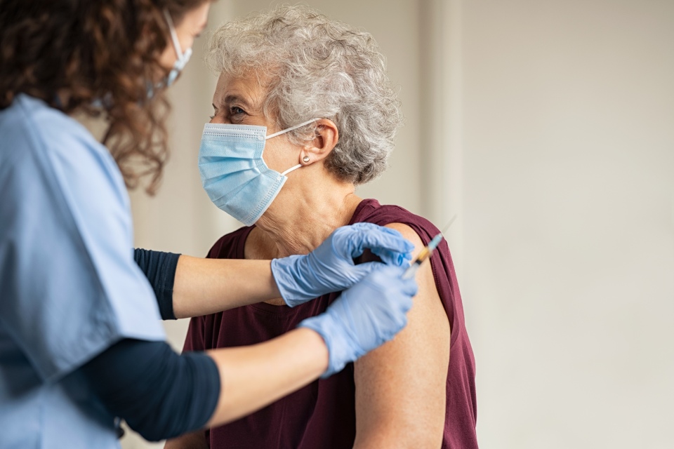 Enfermera con mascarilla pone una inyección en el brazo a una mujer mayor