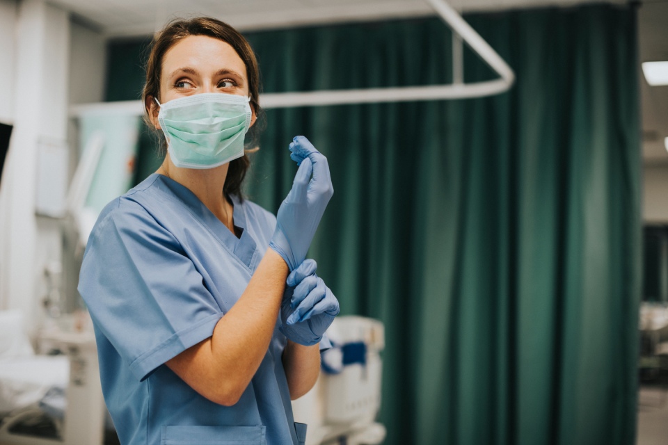 Médica con mascarilla se pone guantes de plástico