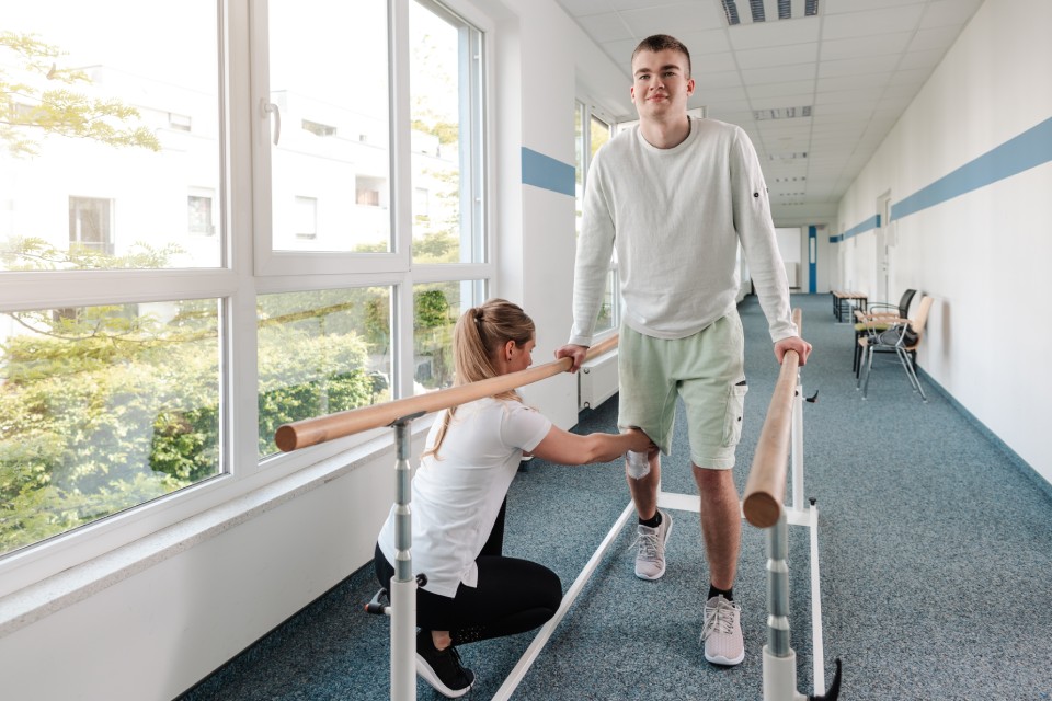 Fisioterapeuta ayuda a hombre a caminar apoyado en barras paralelas