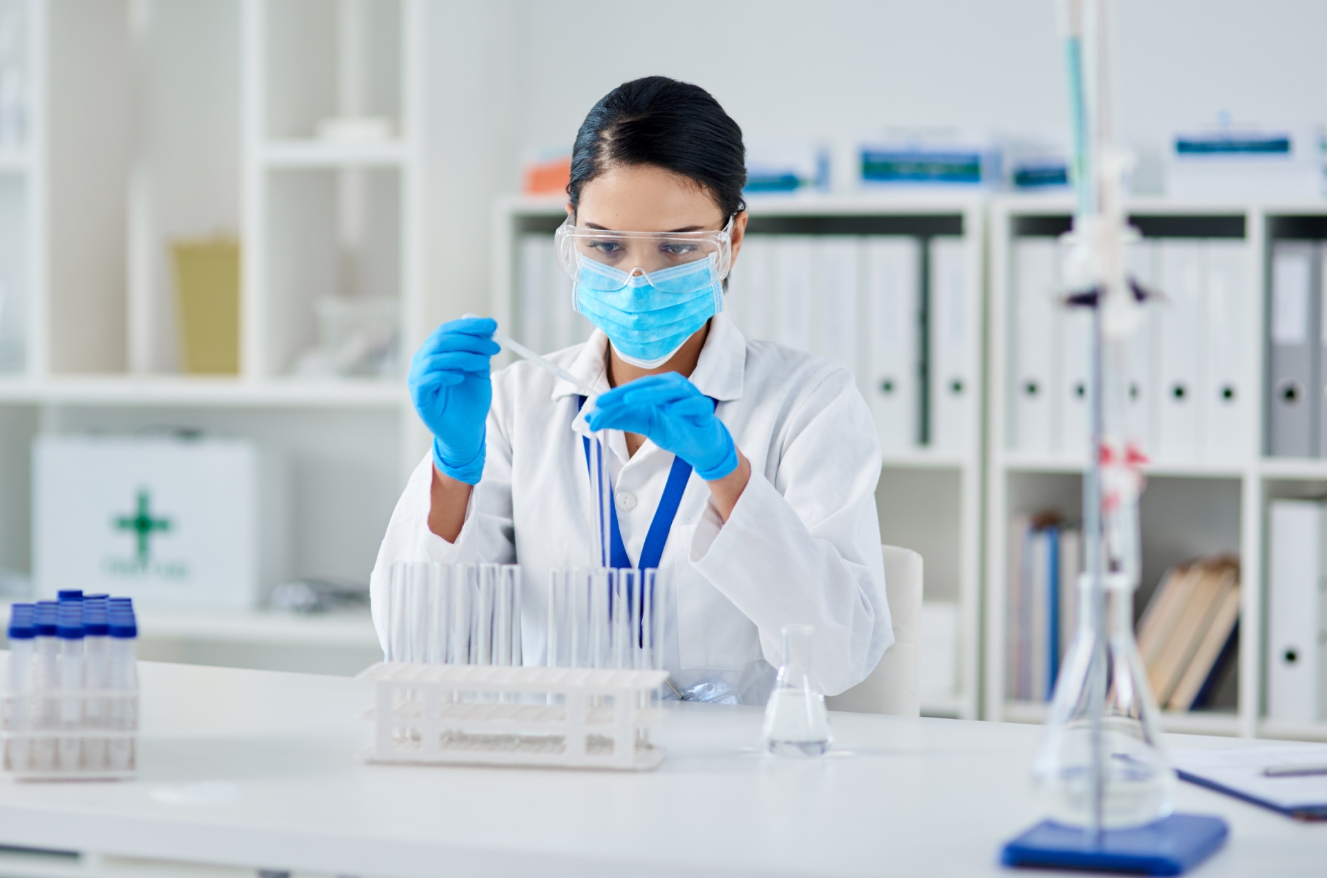 Mujer con bata y mascarilla rellena una pipeta en un laboratorio